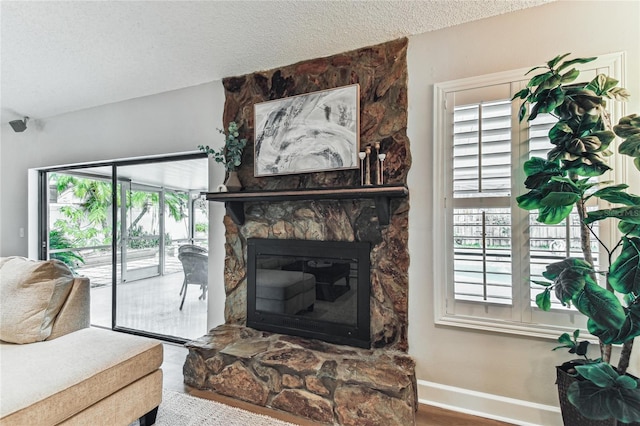 living room with wood-type flooring, a stone fireplace, and a textured ceiling