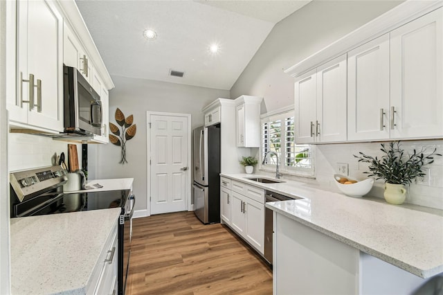 kitchen with lofted ceiling, sink, white cabinetry, appliances with stainless steel finishes, and light stone countertops