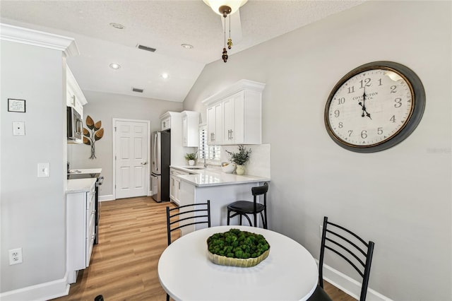 dining room with lofted ceiling, light hardwood / wood-style floors, sink, and a textured ceiling