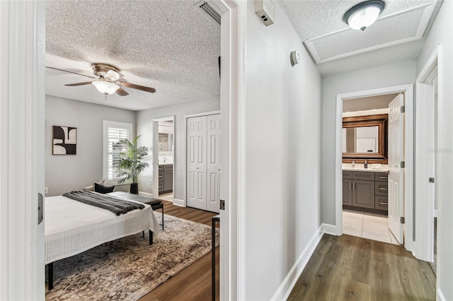 bedroom featuring connected bathroom, hardwood / wood-style floors, a textured ceiling, and ceiling fan