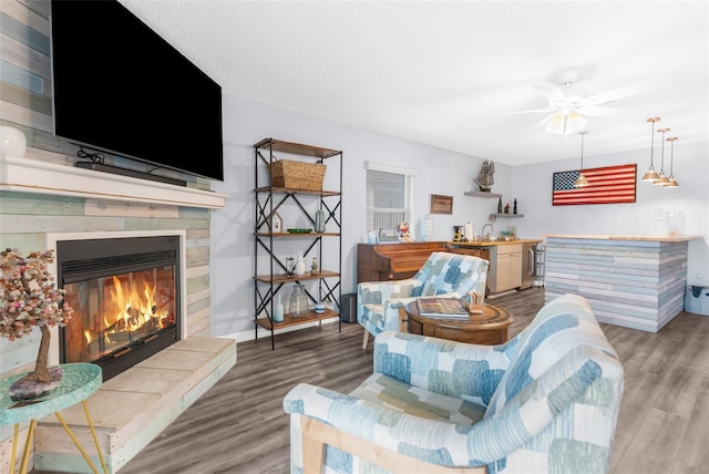 living room featuring a tiled fireplace, wood-type flooring, and indoor wet bar