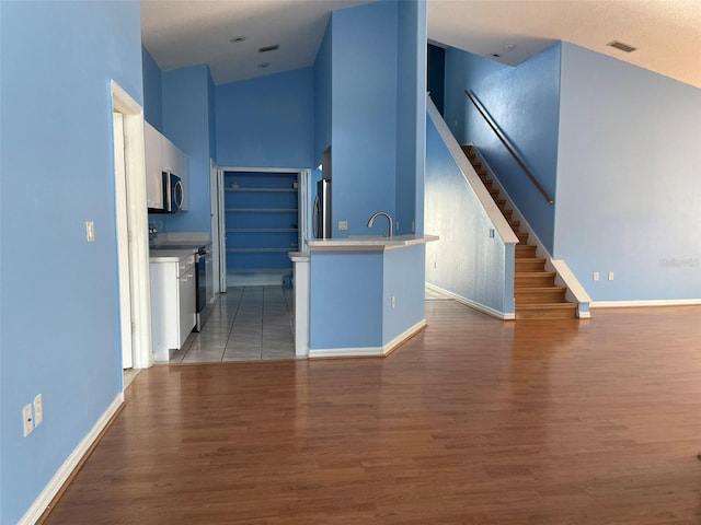 interior space with sink, light hardwood / wood-style flooring, appliances with stainless steel finishes, a kitchen island with sink, and white cabinets