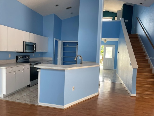 kitchen with appliances with stainless steel finishes, a towering ceiling, white cabinets, and light hardwood / wood-style floors