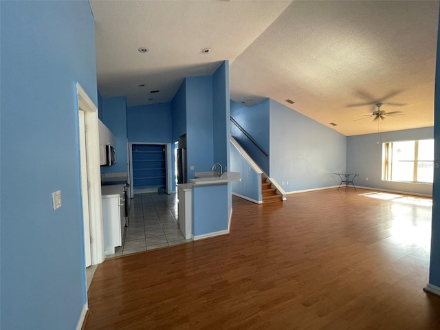 unfurnished living room with ceiling fan, sink, a textured ceiling, and light wood-type flooring