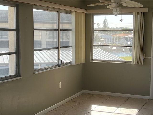 tiled empty room featuring a wealth of natural light, ceiling fan, and a water view