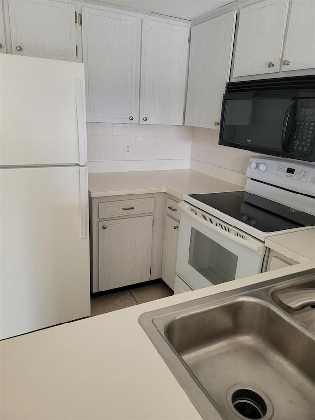 kitchen with light tile patterned floors, sink, white appliances, white cabinets, and decorative backsplash