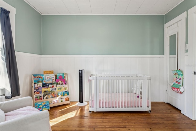 bedroom featuring a crib, wood finished floors, and a wainscoted wall