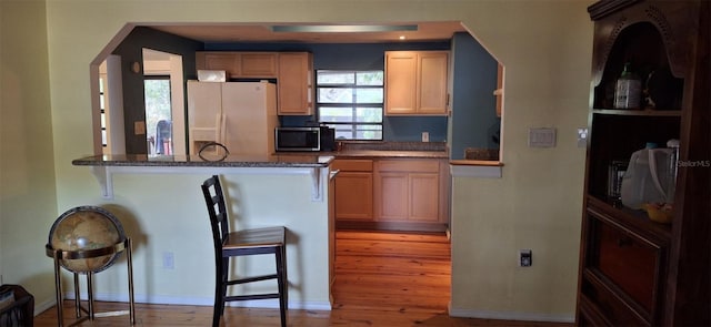 kitchen with a kitchen breakfast bar, kitchen peninsula, fridge with ice dispenser, and light brown cabinets