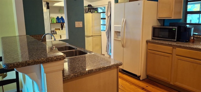 kitchen with sink, a breakfast bar area, dark stone countertops, white fridge with ice dispenser, and light hardwood / wood-style floors