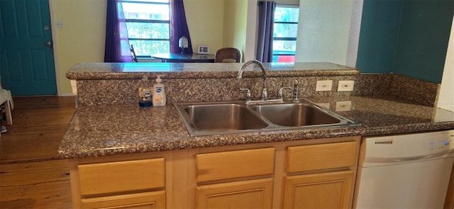 kitchen featuring white dishwasher, sink, light brown cabinetry, and dark stone countertops