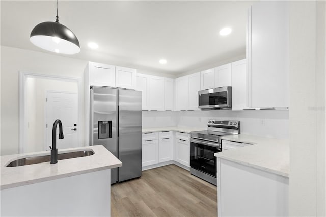 kitchen featuring a sink, light wood-style floors, appliances with stainless steel finishes, white cabinets, and light stone countertops