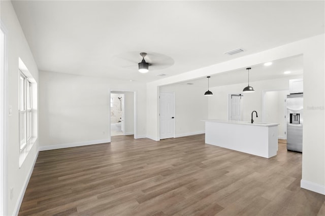 unfurnished living room with visible vents, baseboards, wood finished floors, a ceiling fan, and a sink