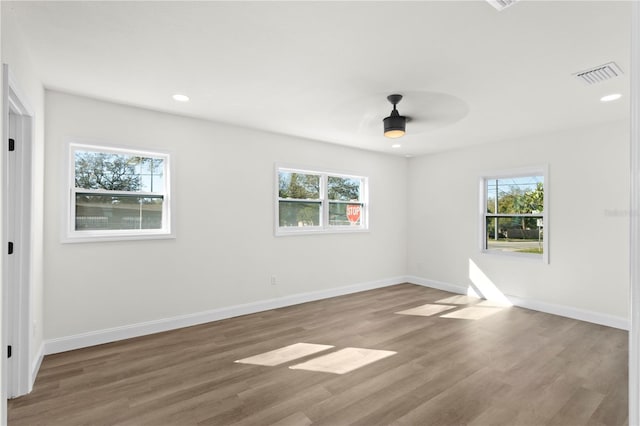 spare room featuring visible vents, plenty of natural light, baseboards, and wood finished floors