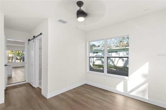 interior space featuring a ceiling fan, wood finished floors, visible vents, baseboards, and a barn door