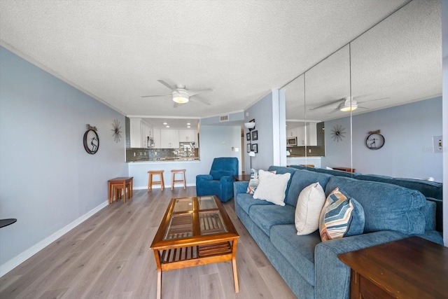 living room with a textured ceiling, ceiling fan, and light wood-type flooring