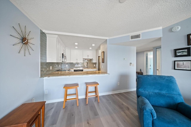 kitchen with a breakfast bar, light wood-type flooring, kitchen peninsula, decorative backsplash, and white cabinets