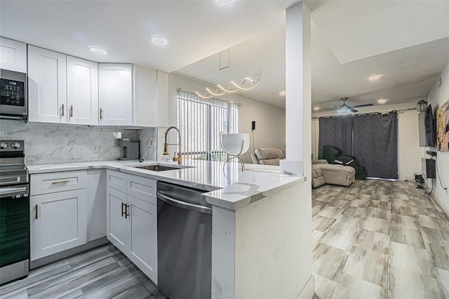 kitchen with sink, light stone counters, kitchen peninsula, stainless steel appliances, and white cabinets