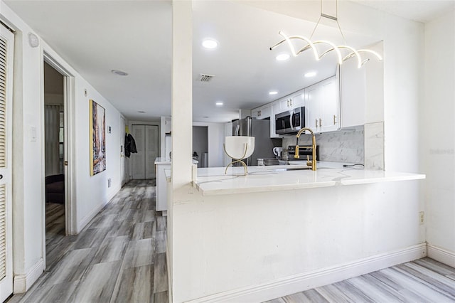 kitchen featuring appliances with stainless steel finishes, white cabinetry, backsplash, kitchen peninsula, and light hardwood / wood-style flooring