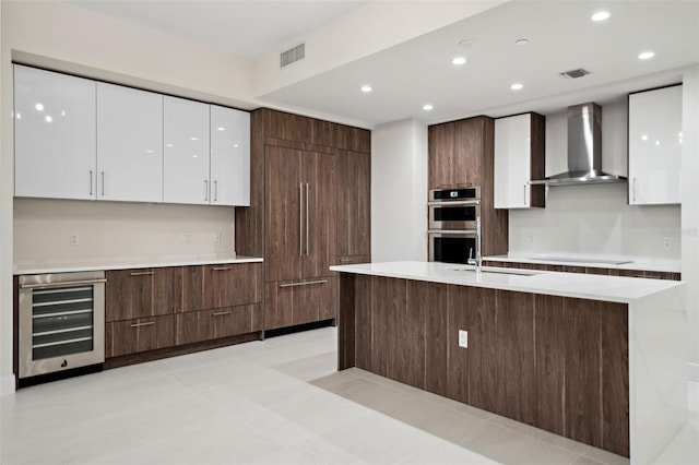 kitchen with white cabinetry, wall chimney range hood, beverage cooler, and double oven