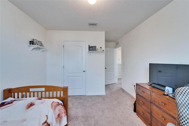 bedroom featuring a textured ceiling, light carpet, visible vents, baseboards, and a closet