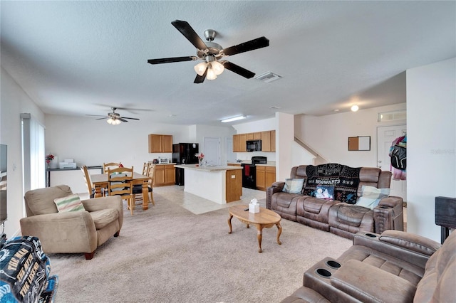 living area featuring light colored carpet, visible vents, ceiling fan, and a textured ceiling