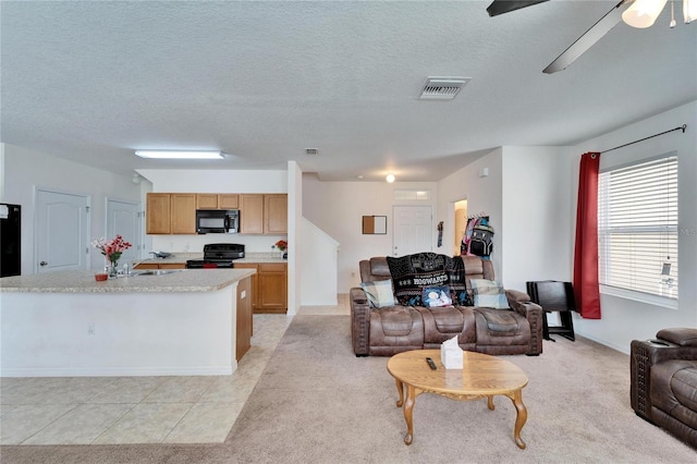 living room featuring a textured ceiling, light tile patterned floors, light colored carpet, visible vents, and a ceiling fan