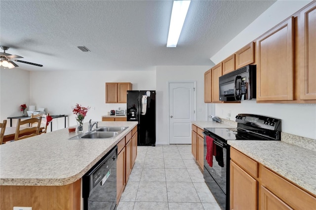 kitchen featuring an island with sink, black appliances, light countertops, and a sink