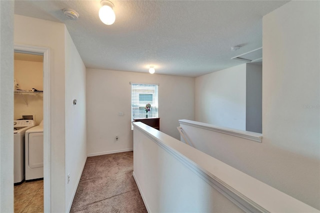 hallway with light colored carpet, attic access, a textured ceiling, an upstairs landing, and washer and dryer