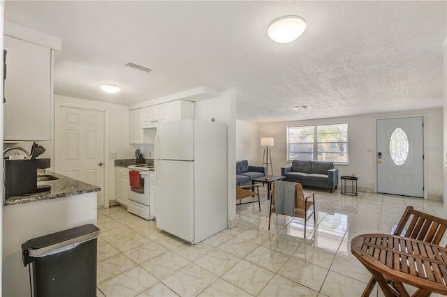 kitchen with white cabinetry, white appliances, a textured ceiling, and dark stone countertops