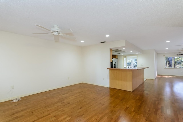 interior space featuring kitchen peninsula, stainless steel fridge, dark hardwood / wood-style floors, and ceiling fan