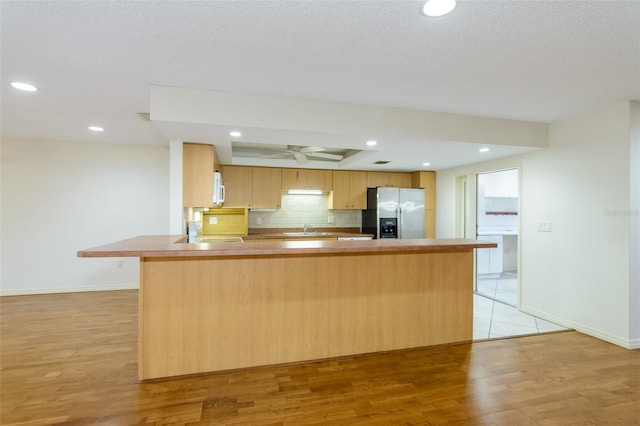 kitchen with light brown cabinetry, sink, decorative backsplash, stainless steel fridge with ice dispenser, and light wood-type flooring