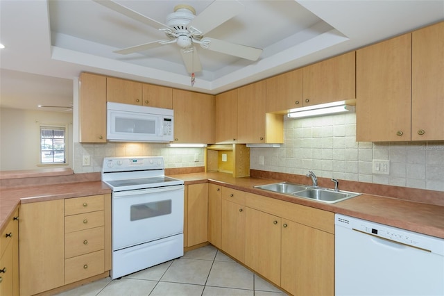 kitchen with a tray ceiling, sink, white appliances, and light tile patterned floors