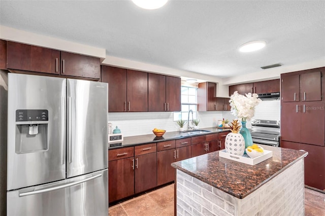 kitchen featuring sink, appliances with stainless steel finishes, dark stone countertops, backsplash, and a center island