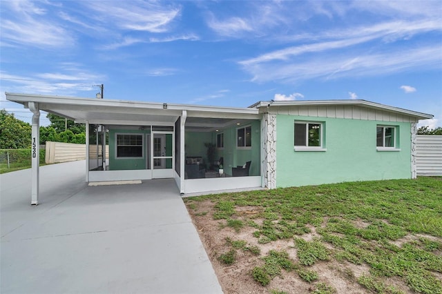 back of property with a carport, a sunroom, and a lawn