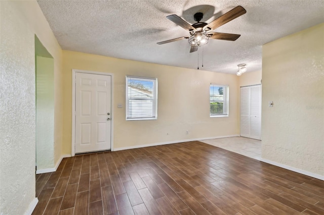 empty room featuring ceiling fan, plenty of natural light, dark hardwood / wood-style floors, and a textured ceiling