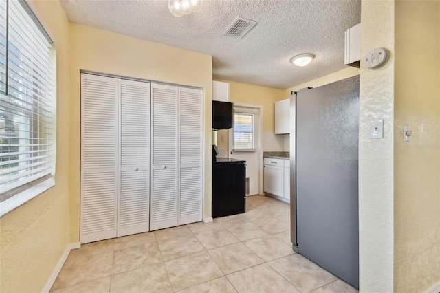 kitchen with a textured ceiling, stainless steel refrigerator, white cabinets, and light tile patterned flooring