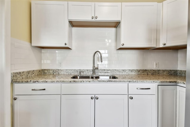 kitchen with white cabinetry, light stone counters, sink, and tasteful backsplash