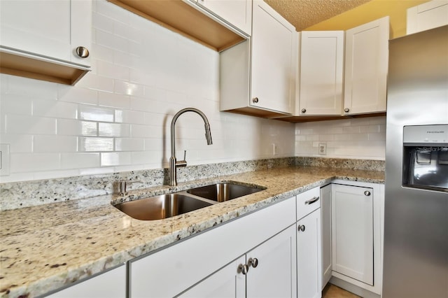 kitchen featuring tasteful backsplash, white cabinetry, sink, stainless steel refrigerator with ice dispenser, and light stone countertops