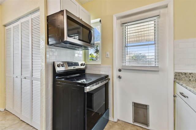 kitchen featuring appliances with stainless steel finishes, white cabinetry, backsplash, light stone countertops, and light tile patterned flooring