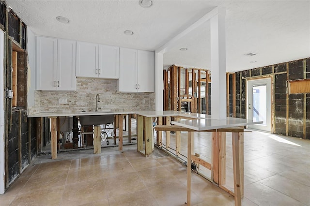 kitchen with a breakfast bar, sink, white cabinetry, a textured ceiling, and decorative backsplash