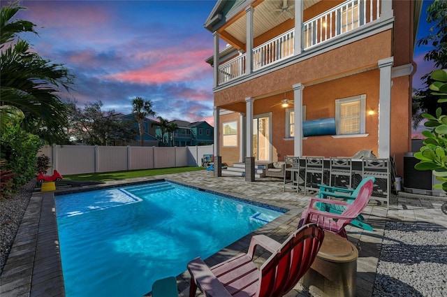 pool at dusk with ceiling fan and a patio