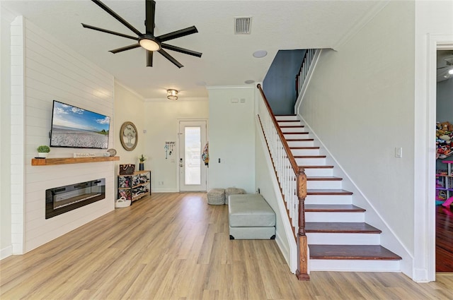 interior space with crown molding, a large fireplace, ceiling fan, and light wood-type flooring