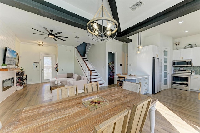 dining room featuring a large fireplace, beam ceiling, and light hardwood / wood-style floors