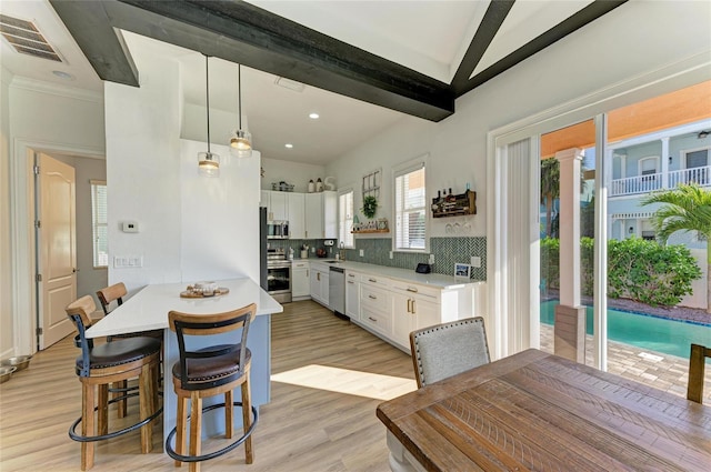 kitchen with beamed ceiling, white cabinetry, backsplash, hanging light fixtures, and stainless steel appliances