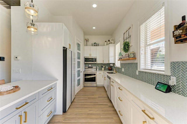 kitchen featuring stainless steel appliances, white cabinetry, pendant lighting, and light wood-type flooring