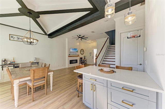 kitchen featuring a breakfast bar area, gray cabinets, hanging light fixtures, a large fireplace, and light wood-type flooring