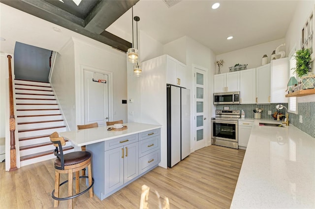 kitchen featuring pendant lighting, white cabinetry, sink, a kitchen bar, and stainless steel appliances