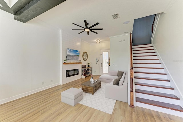 living room with ceiling fan, a large fireplace, crown molding, and light wood-type flooring