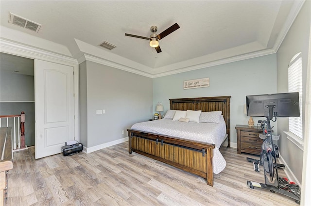 bedroom featuring ceiling fan, ornamental molding, a tray ceiling, and light hardwood / wood-style flooring