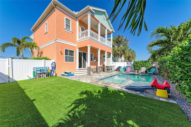 rear view of property with a balcony, a yard, a fenced in pool, and a patio area